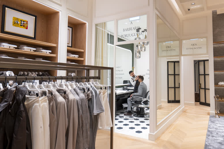 Sacoor Brothers Mall of the Emirates boutique interior, featuring tailored menswear displays, warm timber shelving, and the entrance to A Barbearia Portuguesa.